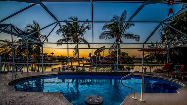 Zona de piscina con techo de cristal, palmeras y vistas al atardecer.