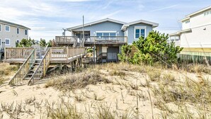 Une maison située en bord de mer, dotée d’une terrasse en bois et d’un escalier menant à un balcon.