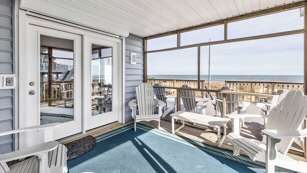 Un espace extérieur abrité, avec des fauteuils Adirondack blancs, une petite table et une vue sur l’océan.