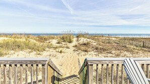 Une promenade en bois qui mène à une plage bordée de dunes et dotée d’une végétation clairsemée.