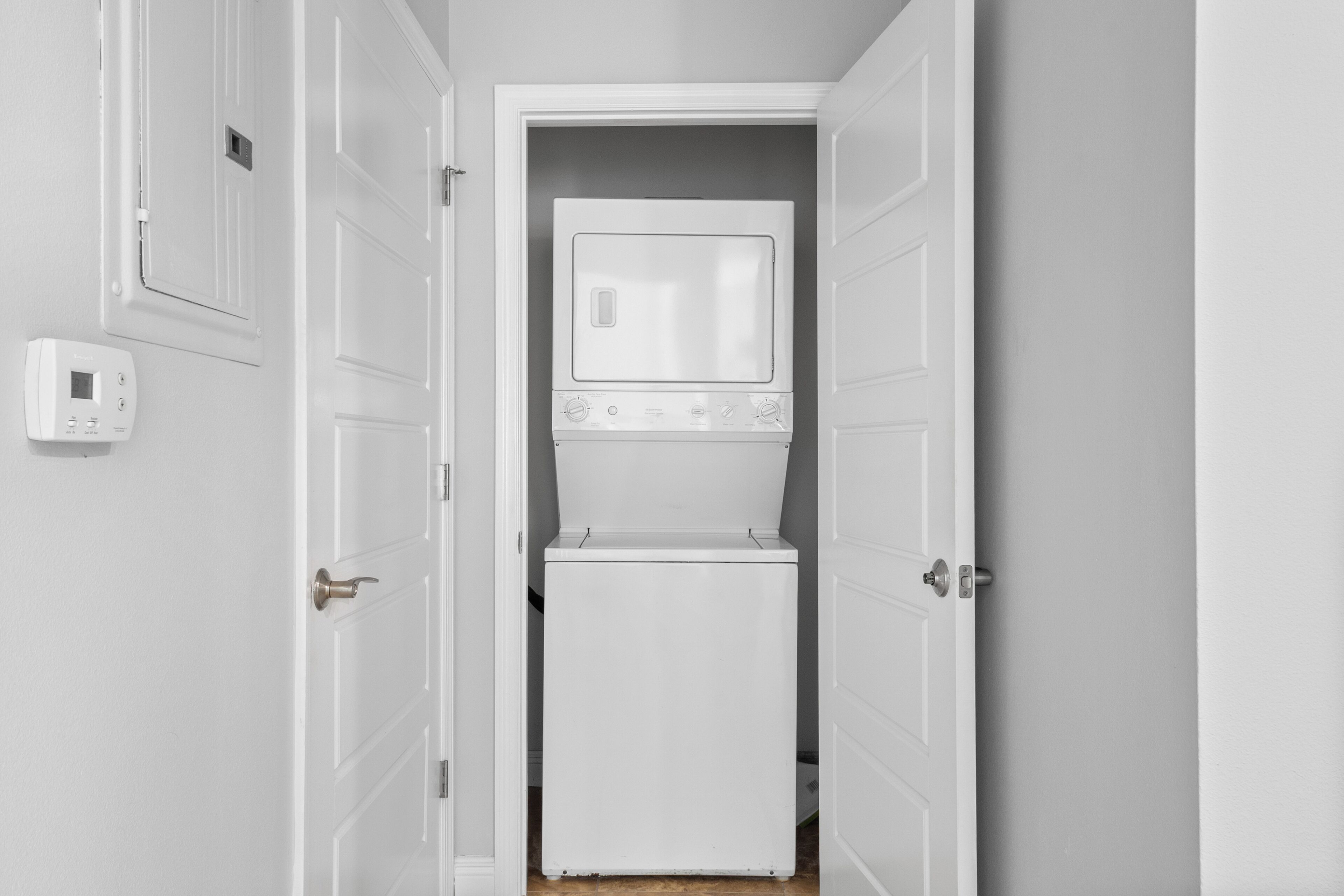 Une buanderie équipée d’un lave-linge et d’un sèche-linge, d’un thermostat et de portes blanches.