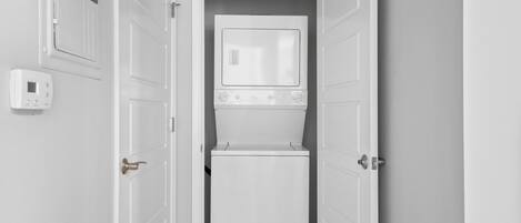 Une buanderie équipée d’un lave-linge et d’un sèche-linge, d’un thermostat et de portes blanches.