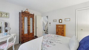A bedroom with a bed, a dresser, a vanity with a mirror, and a staircase leading to another floor.