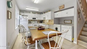 A compact kitchen with white cabinets, a wooden dining table, and a washing machine.