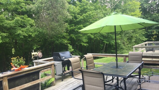 An outdoor deck with a grill, a table, chairs, and an umbrella.