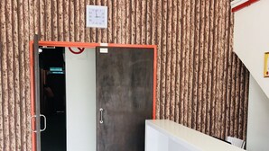 A reception area with a wooden textured wall, a reception desk, and a door leading to another room. - H-Hotel (Johor Bahru)