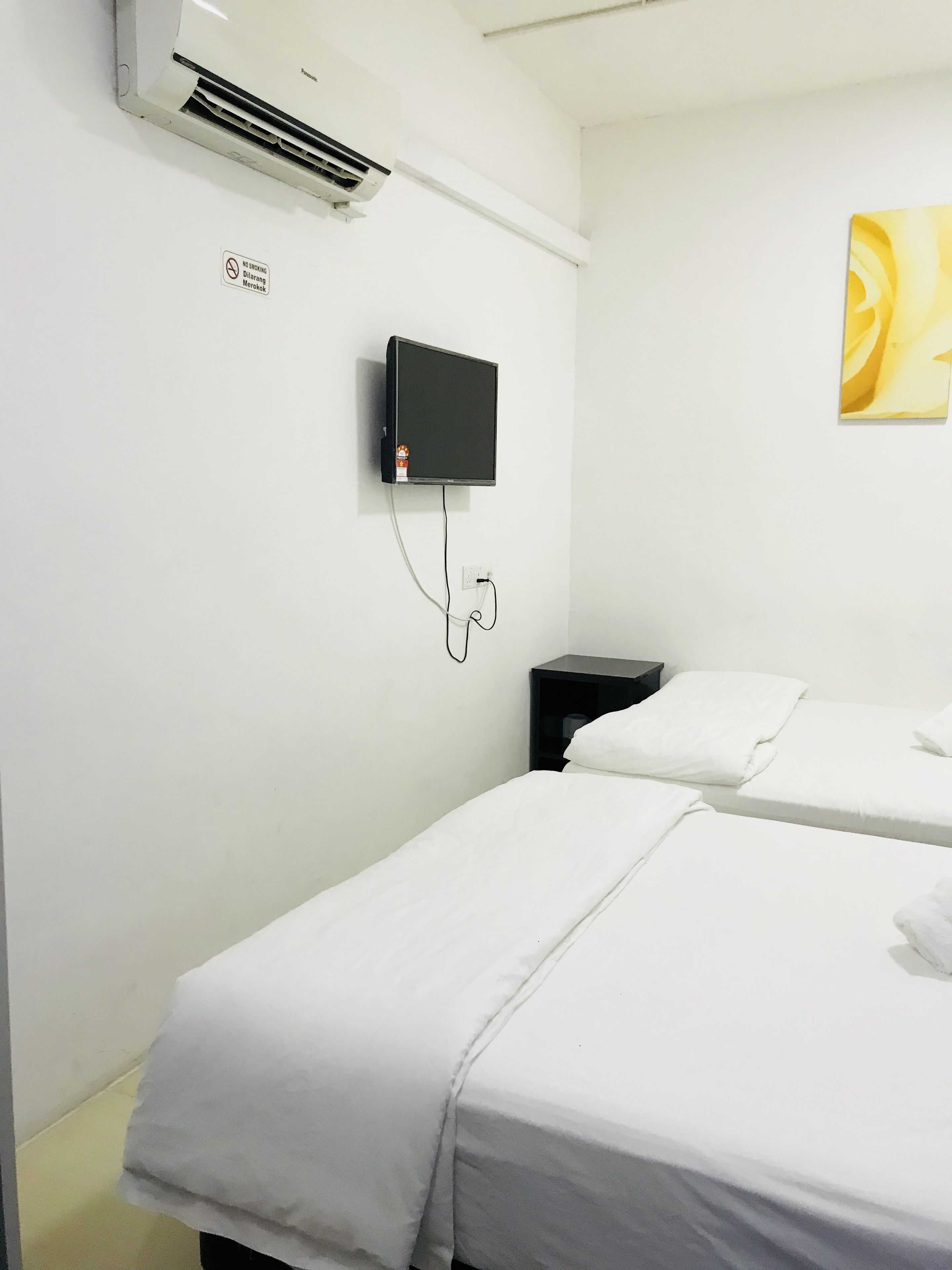 A hotel room with two beds, a mounted TV, an air conditioning unit, and a power outlet.