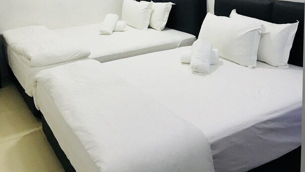 A hotel room with three single beds, white bedding, and two yellow floral wall art pieces. - H-Hotel (Johor Bahru)