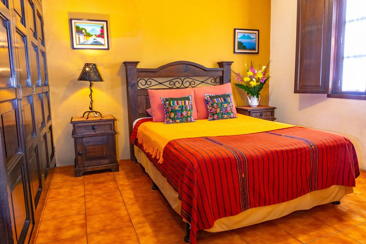 Un dormitorio con una cama de madera, una mesita de noche con una lámpara y un florero con flores.