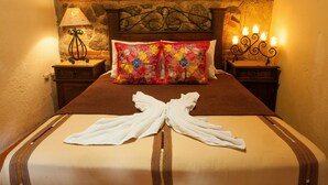 Un lit bien fait, agrémenté d’un coussin décoratif, d’une serviette joliment disposée et d’une tête de lit adossée à un mur en pierre.