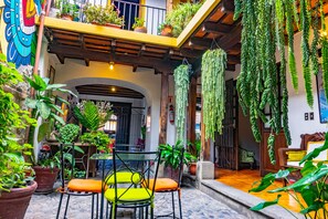 A courtyard with potted plants, a table with chairs, and hanging plants. - Hotel Palacio Chico 1940 (Antigua Guatemala)