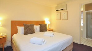 Ein Hotelzimmer mit einem großen Bett, zwei Kissen, einer Nachttischlampe, einem Telefon auf dem Nachttisch und einer Klimaanlage an der Wand.