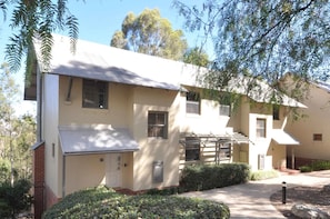 A two-story building with a flat roof, a front porch, and a small garden area.