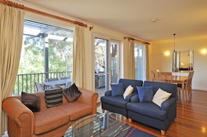 A living room with a sofa, a glass coffee table, and a dining area with a table and chairs. - Petit Verdot 2BR Villa within Cypress Lakes Resort (Pokolbin)