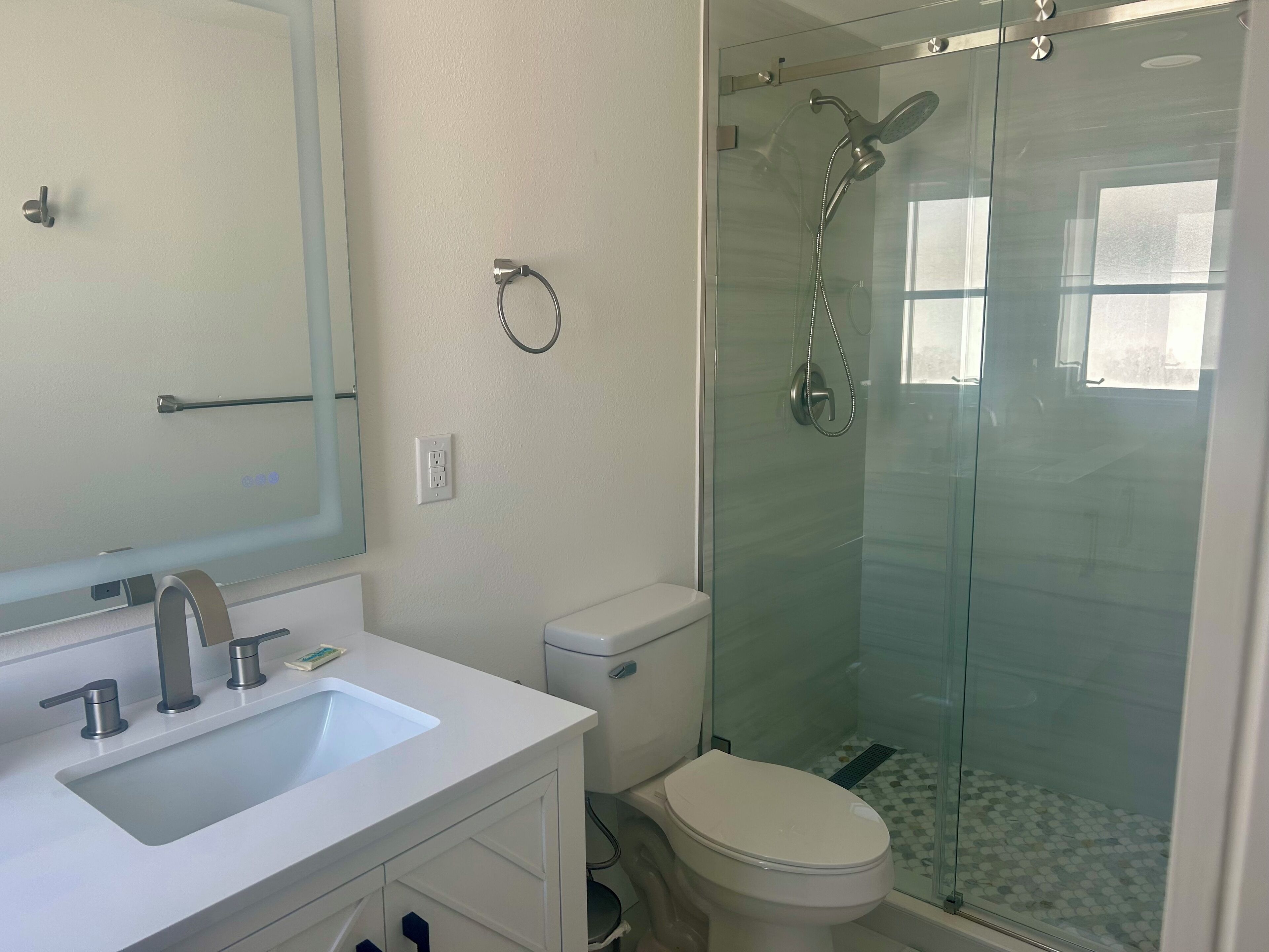 Une salle de bain avec un lavabo blanc, des toilettes et une douche séparée par une paroi de verre.