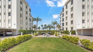 A residential building with multiple floors, a central courtyard with grass and palm trees, and a car parked on the left. - Island House Beach Resort V8 (Siesta Key)