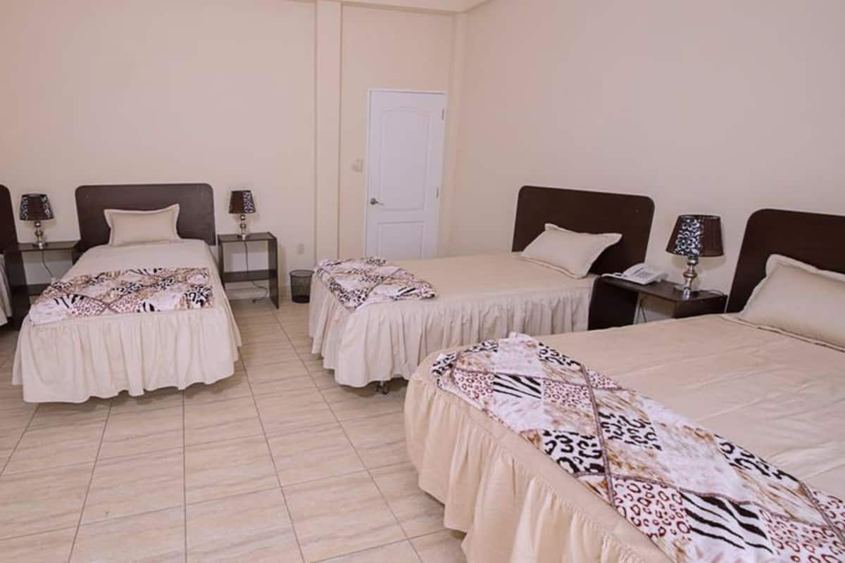 Une chambre d’hôtel avec quatre lits, chacun recouvert d’une couvre-lit à motifs et doté d’une table de chevet avec une lampe.