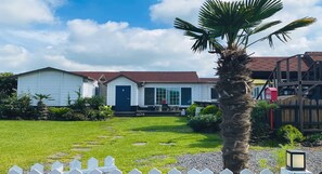 A white single-story house with a red roof, a front porch, and a palm tree in the yard. - Haepumdal Pension (Jeju City)