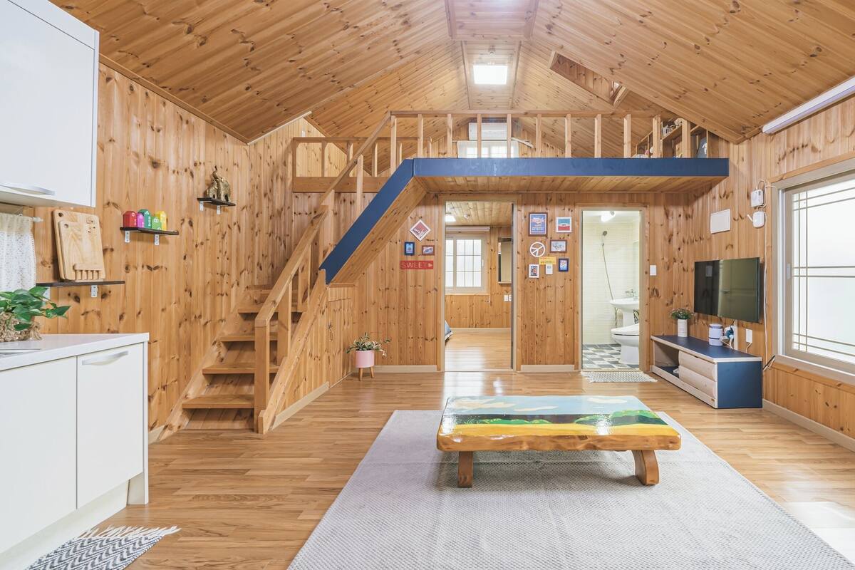 A wooden interior with a staircase, a dining table, and a TV.
