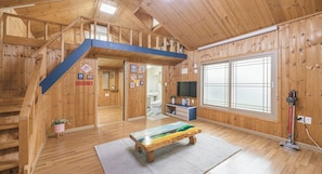 A wooden cabin interior with a loft bedroom, a dining area, and a bathroom. - Haepumdal Pension (Jeju City)