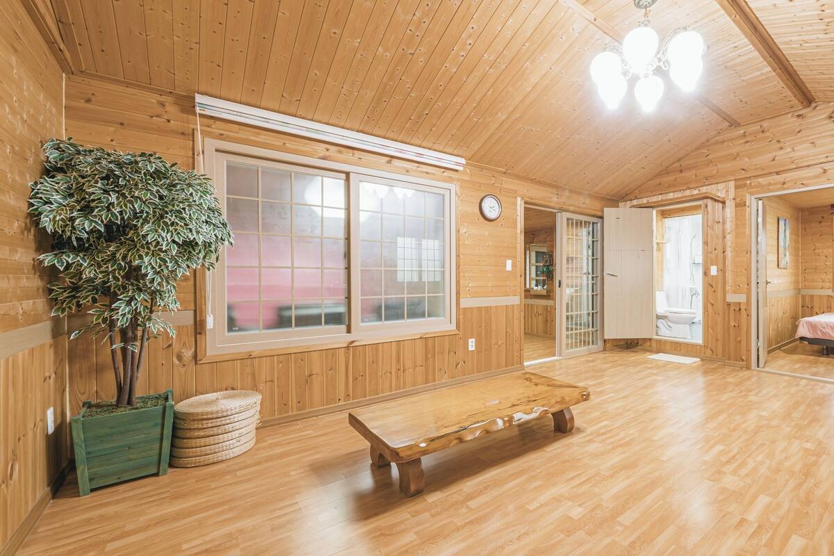 A wooden interior with large windows, a wooden bench, and a potted plant.