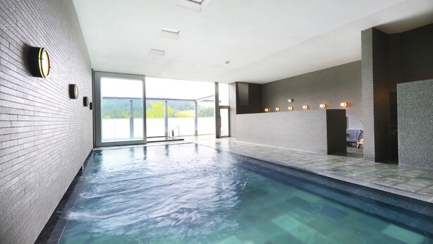 A large indoor swimming pool with clear water, a tiled floor, and a view of greenery outside. - Menard Aoyama Resort Hotel Schönvert (Iga)