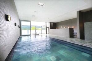 Une grande piscine intérieure à l’eau claire, dotée d’un sol carrelé et offrant une vue sur la verdure environnante.
