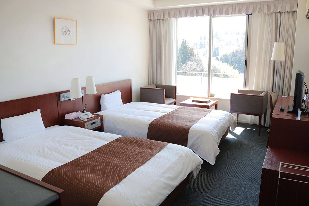 Habitación de hotel con dos camas, un escritorio, una silla, un televisor y una ventana con vista a árboles.