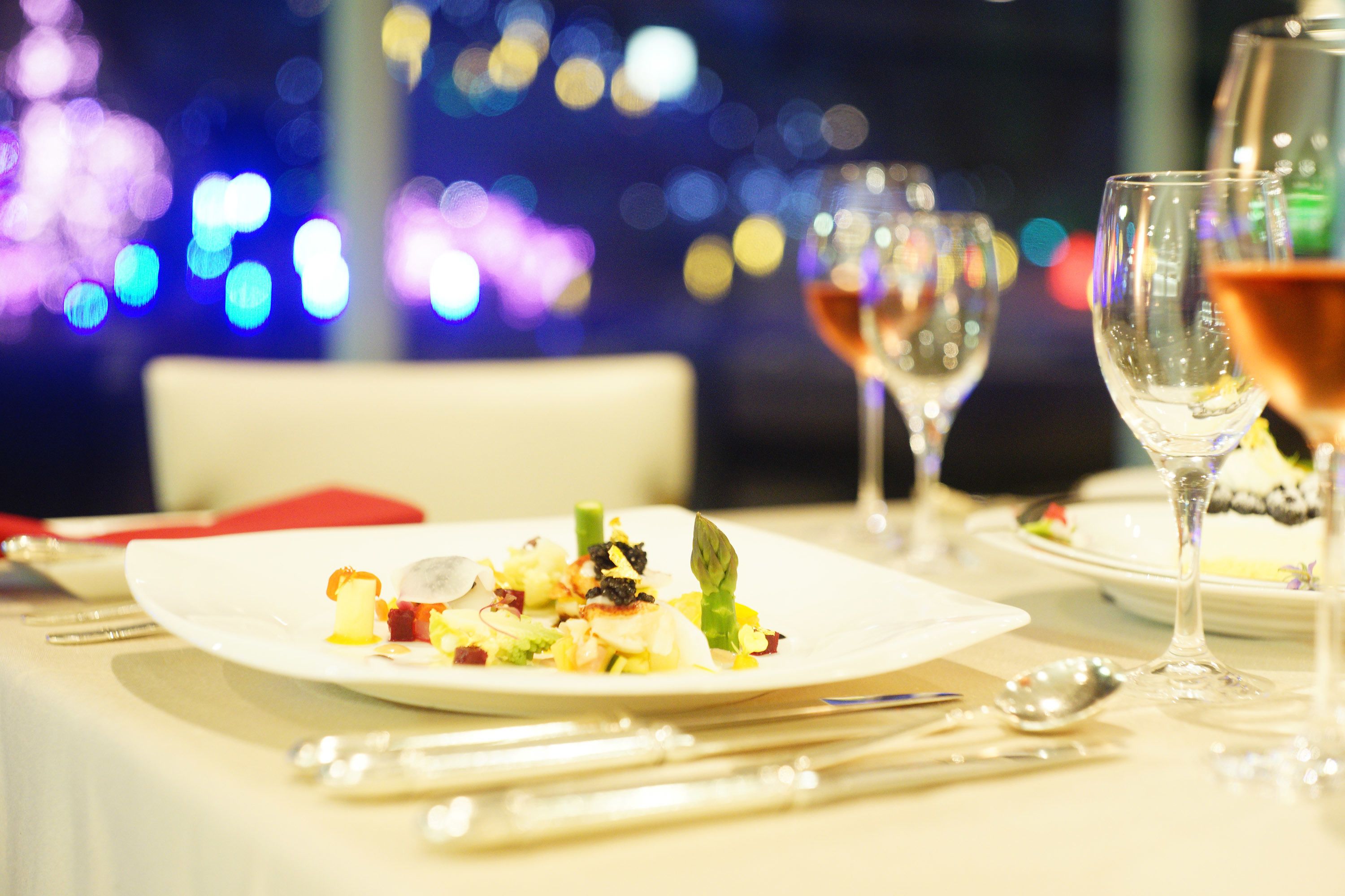 A dining table set with plates, cutlery, and glasses, with a cityscape view in the background.