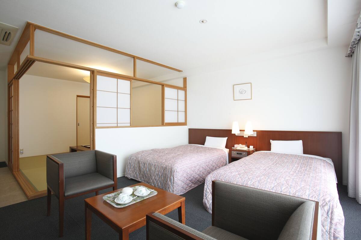 Una habitación de hotel con dos camas, un escritorio, una silla y una mesita con bandeja.