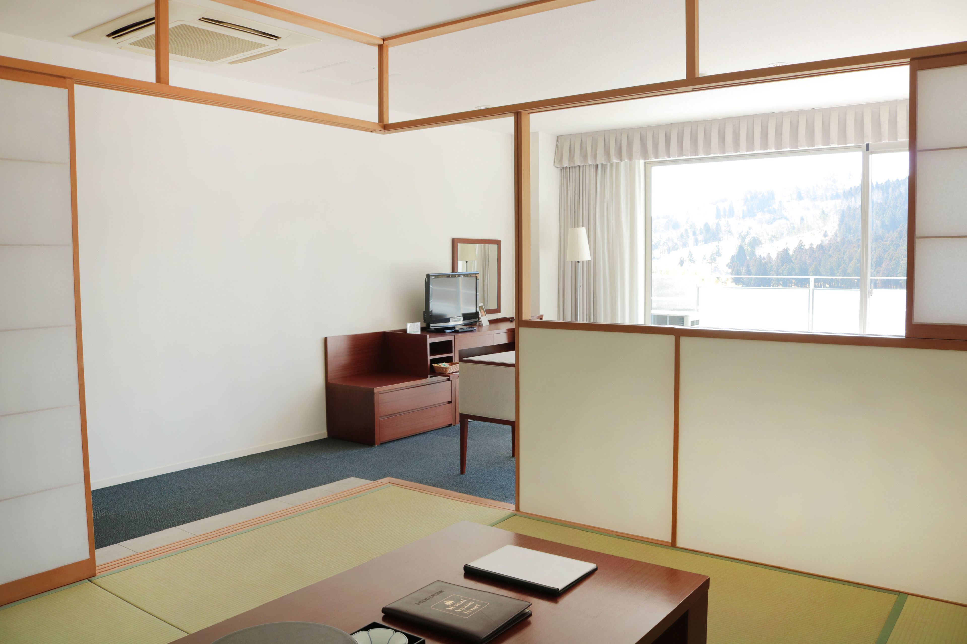 Une chambre d’hôtel équipée d’un bureau, d’une chaise et d’un téléviseur. Une fenêtre offre une vue sur une montagne.