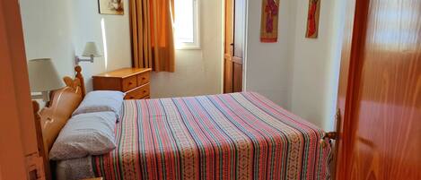 Camera da letto con un letto, una testiera in legno, un comodino, una lampada, una finestra con tende e decorazioni a parete.