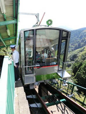A cable car with passengers, a guard, and a scenic view of a forested mountain area.