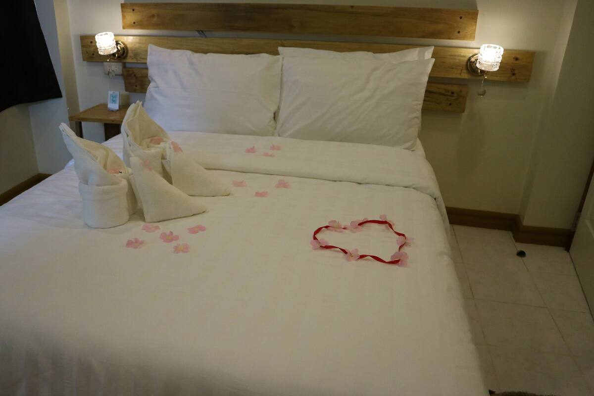 A neatly made bed with white linens, pillows, and a heart-shaped decoration on the bedspread.