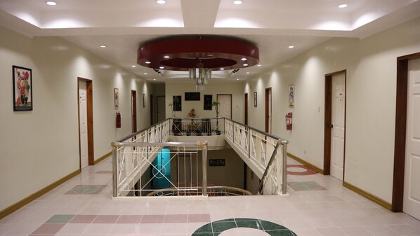 A spacious hallway with a central staircase, white walls, and a tiled floor.