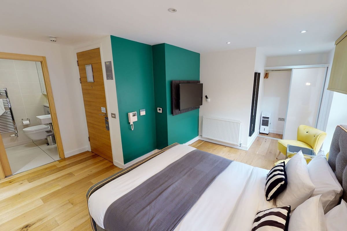 A modern hotel room with a bed, a television, a bathroom, and a seating area.