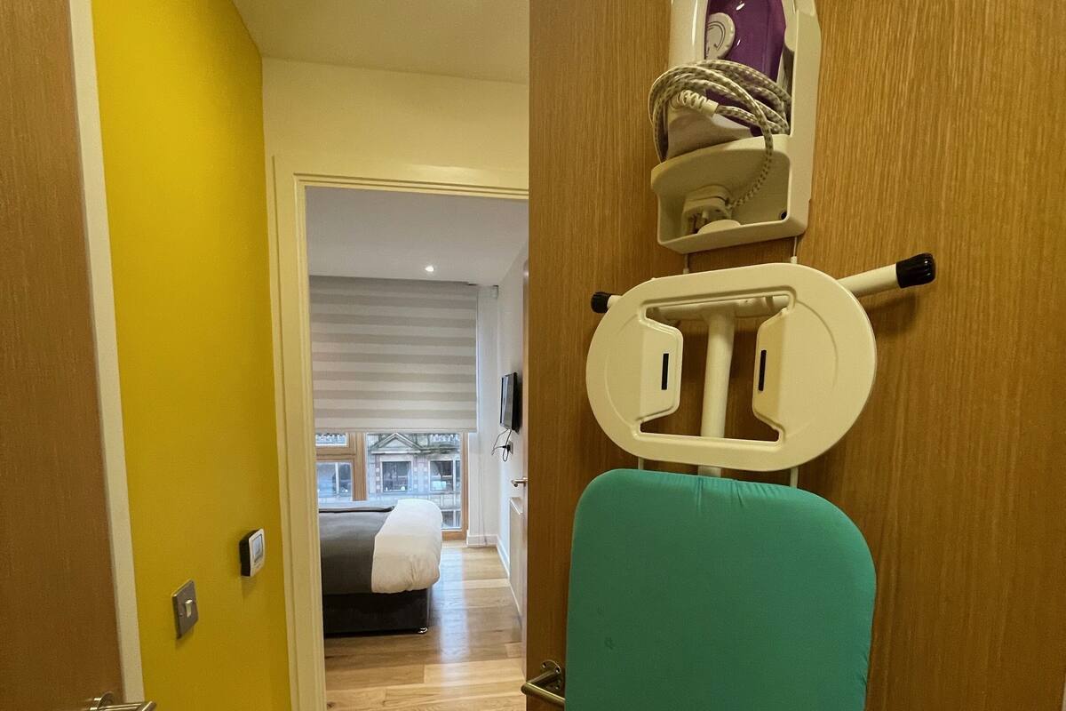 A hallway with a wooden door, a teal ironing board, and a ceiling light.