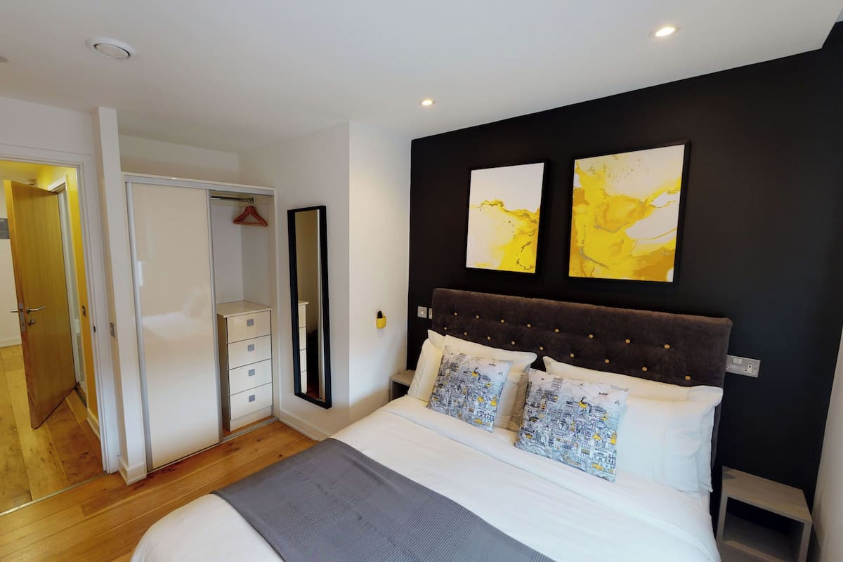 A bedroom with a bed, a wardrobe, a mirror, and two abstract paintings on the wall.