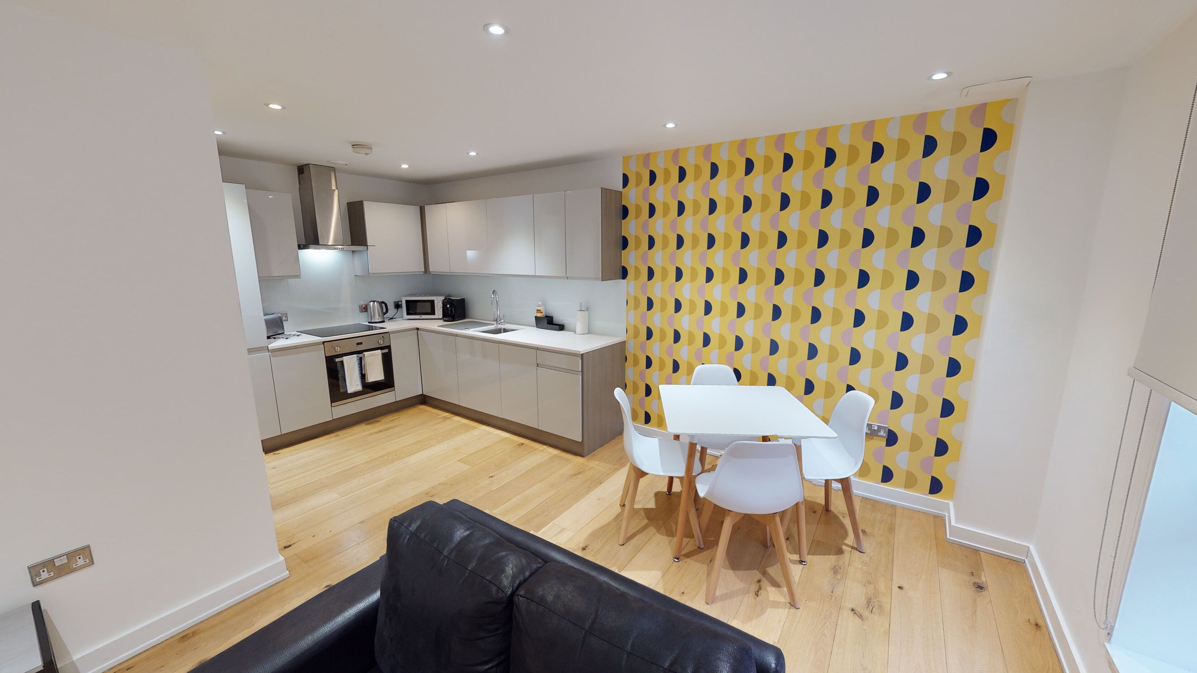 A modern kitchen with white cabinets, a dining area with a white table and chairs, and a patterned wall.