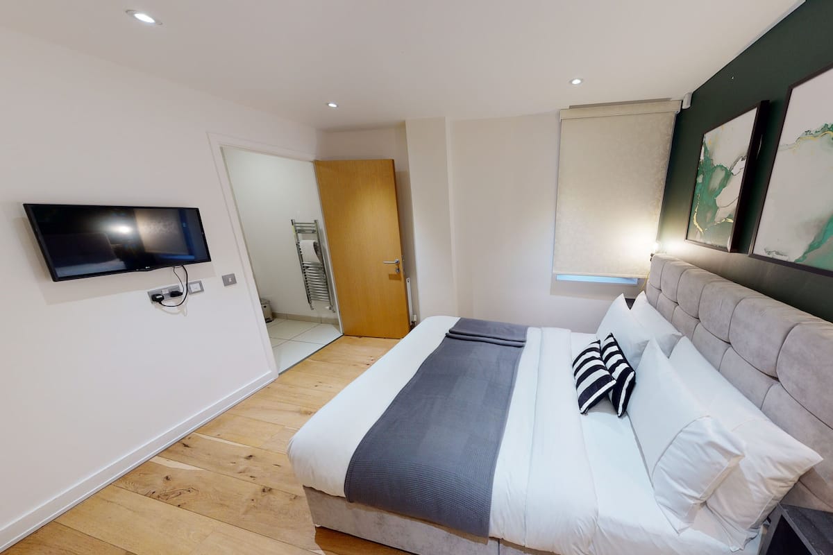 A modern hotel room with a large bed, a flat-screen TV mounted on the wall, and artwork on the walls.