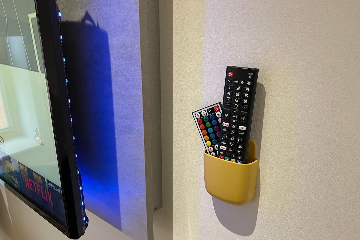 A wall-mounted TV with a remote control holder containing two remotes.