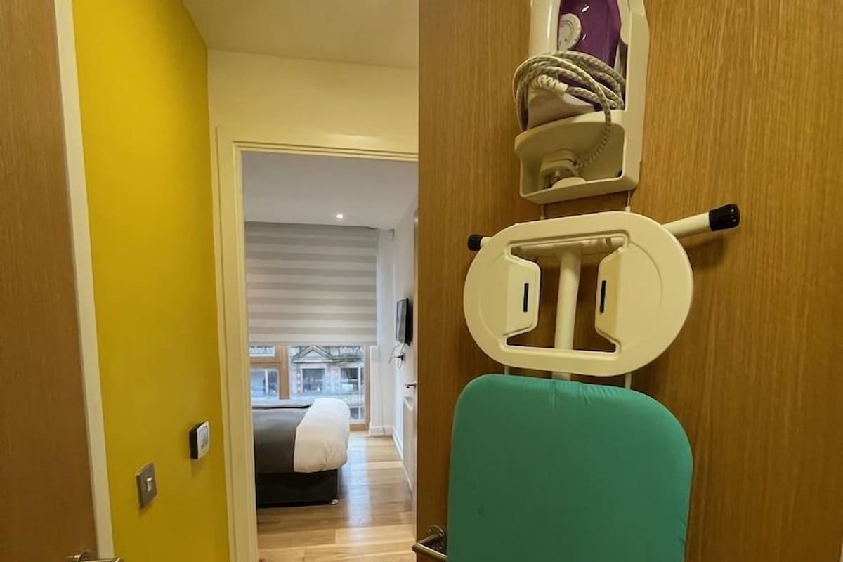 A hallway with a wooden door, a teal ironing board, and a ceiling light.