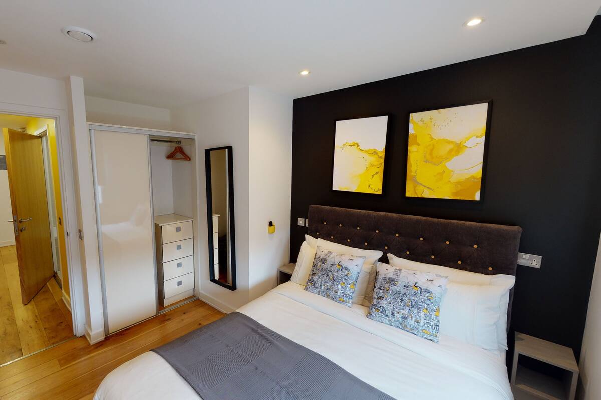 A modern bedroom with a large bed, a wardrobe, and a mirror.