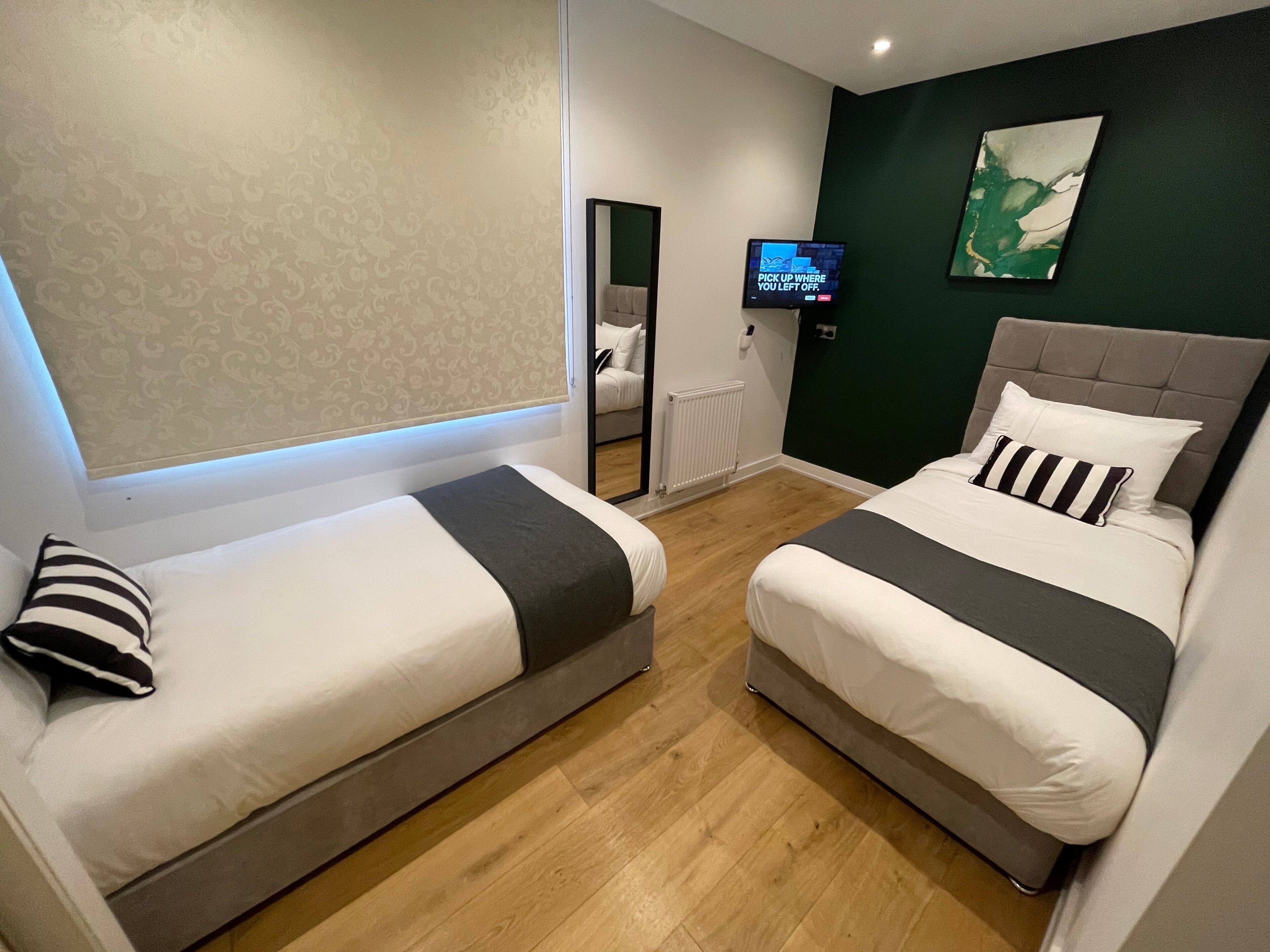 A hotel room with two beds, a television, and a green accent wall.