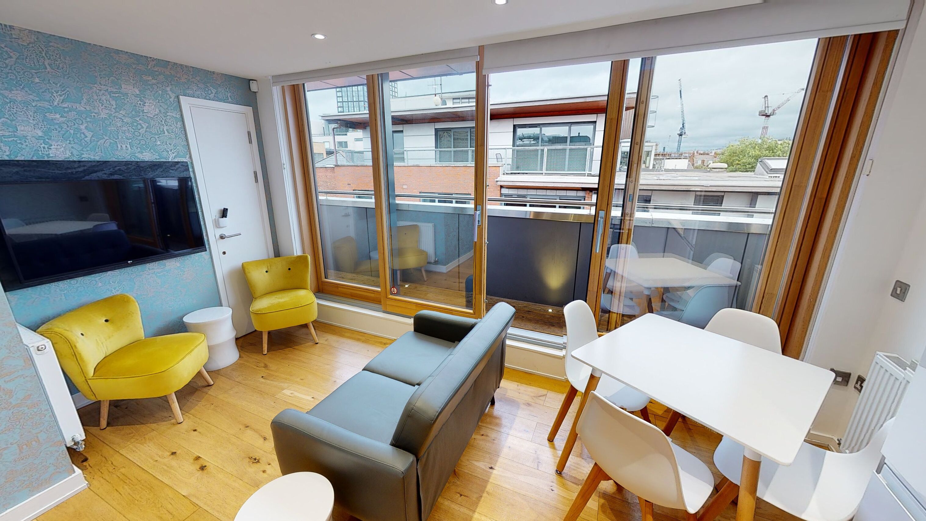 Uma sala de estar moderna com sofá, poltronas amarelas, uma mesa de jantar e grandes janelas com vista para a paisagem urbana.