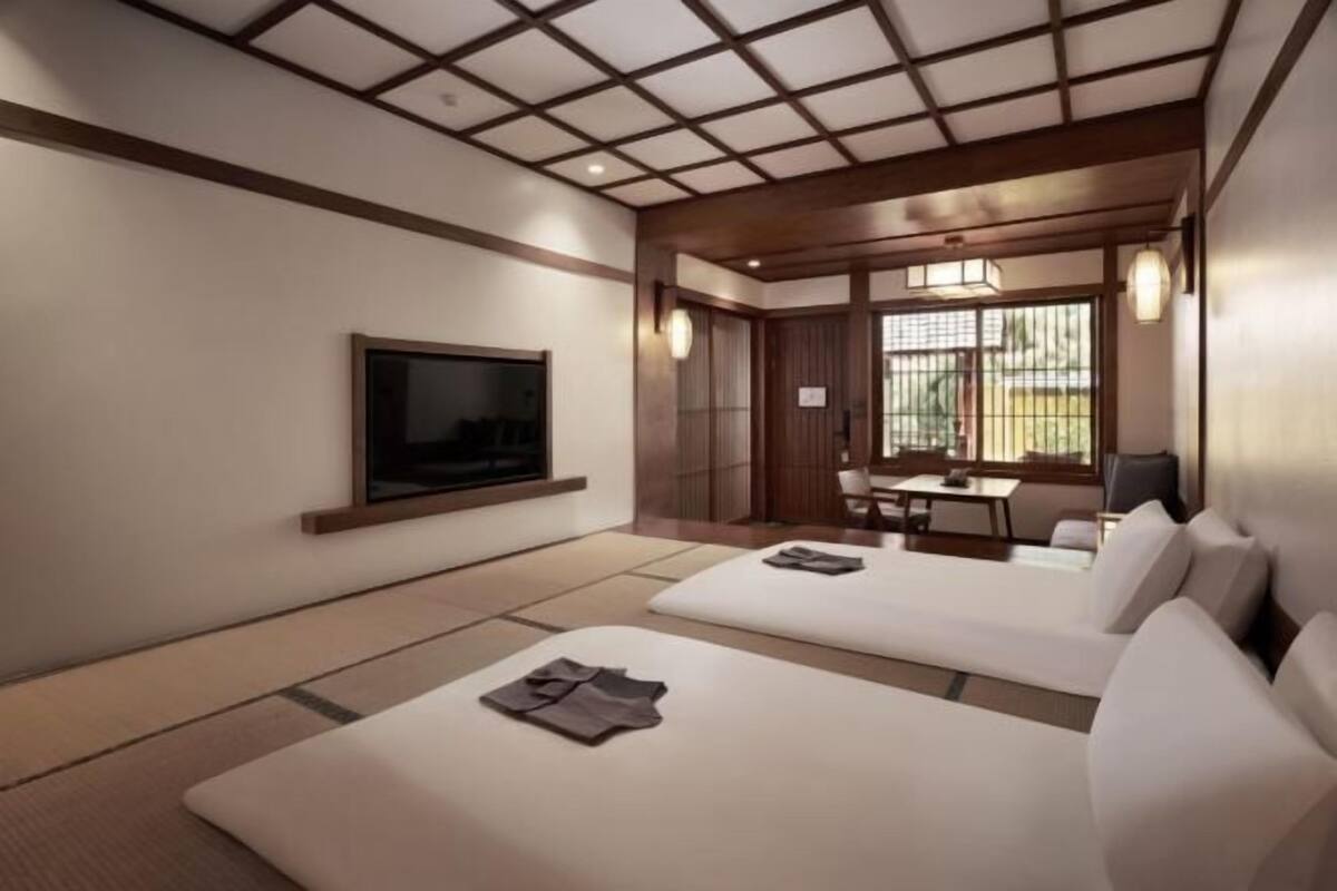 A modern hotel room with a large flat-screen TV, a sofa, a dining area, and a traditional Japanese-style sliding door.