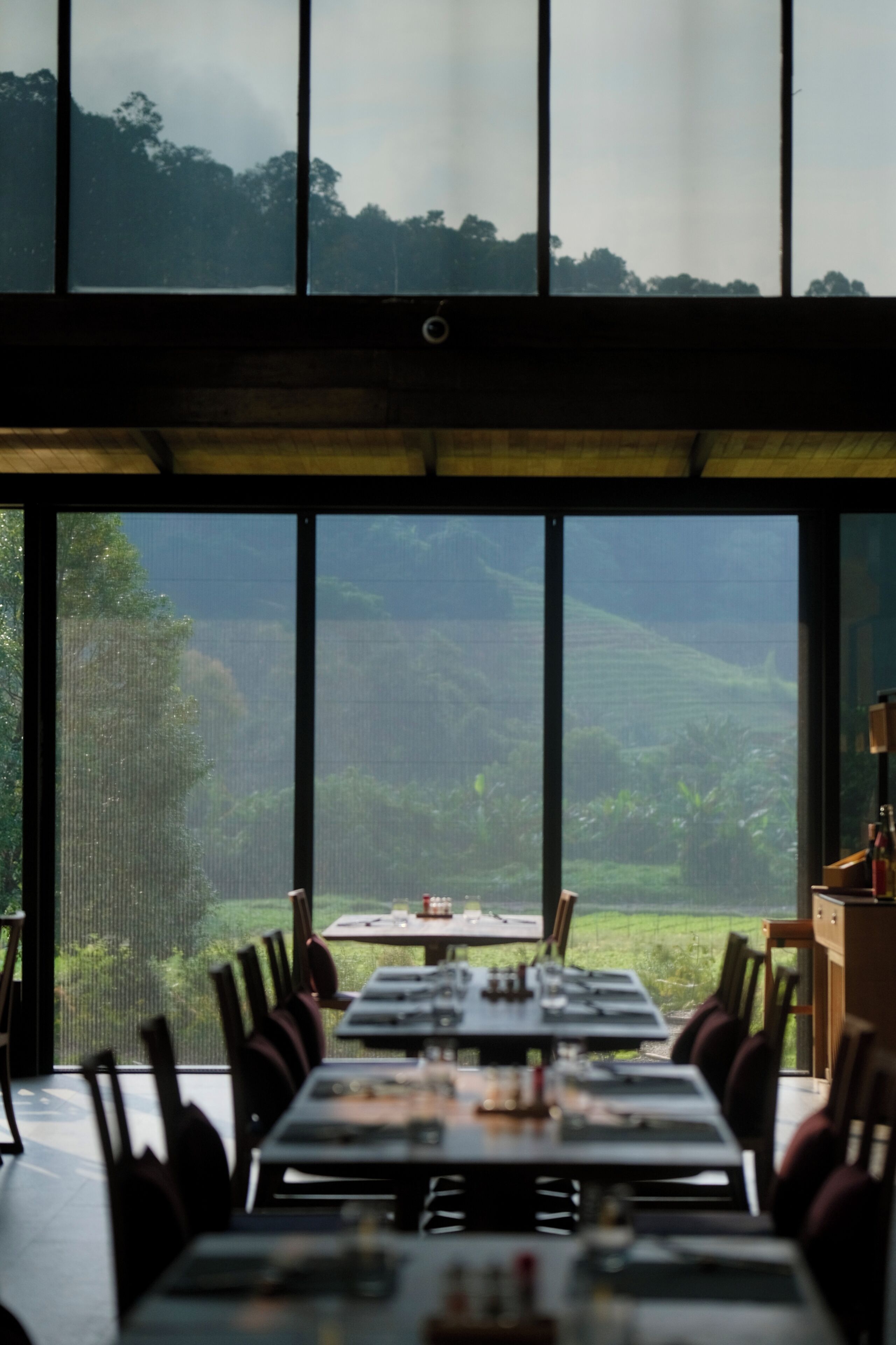 Comedor con una mesa lista para cuatro personas, grandes ventanales con vistas a un paisaje verde.