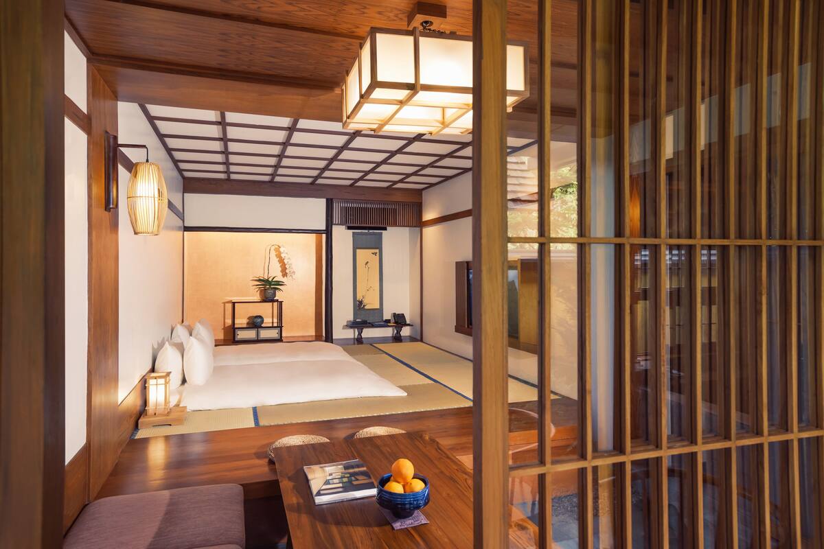 A traditional Japanese room with tatami flooring, a low table with a book and fruit, a hanging lantern, and a sliding door.
