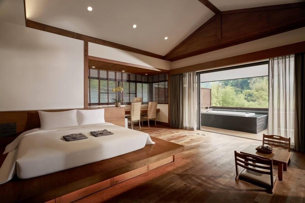A modern bedroom with a large bed, a dining table, and a view of a hot tub.