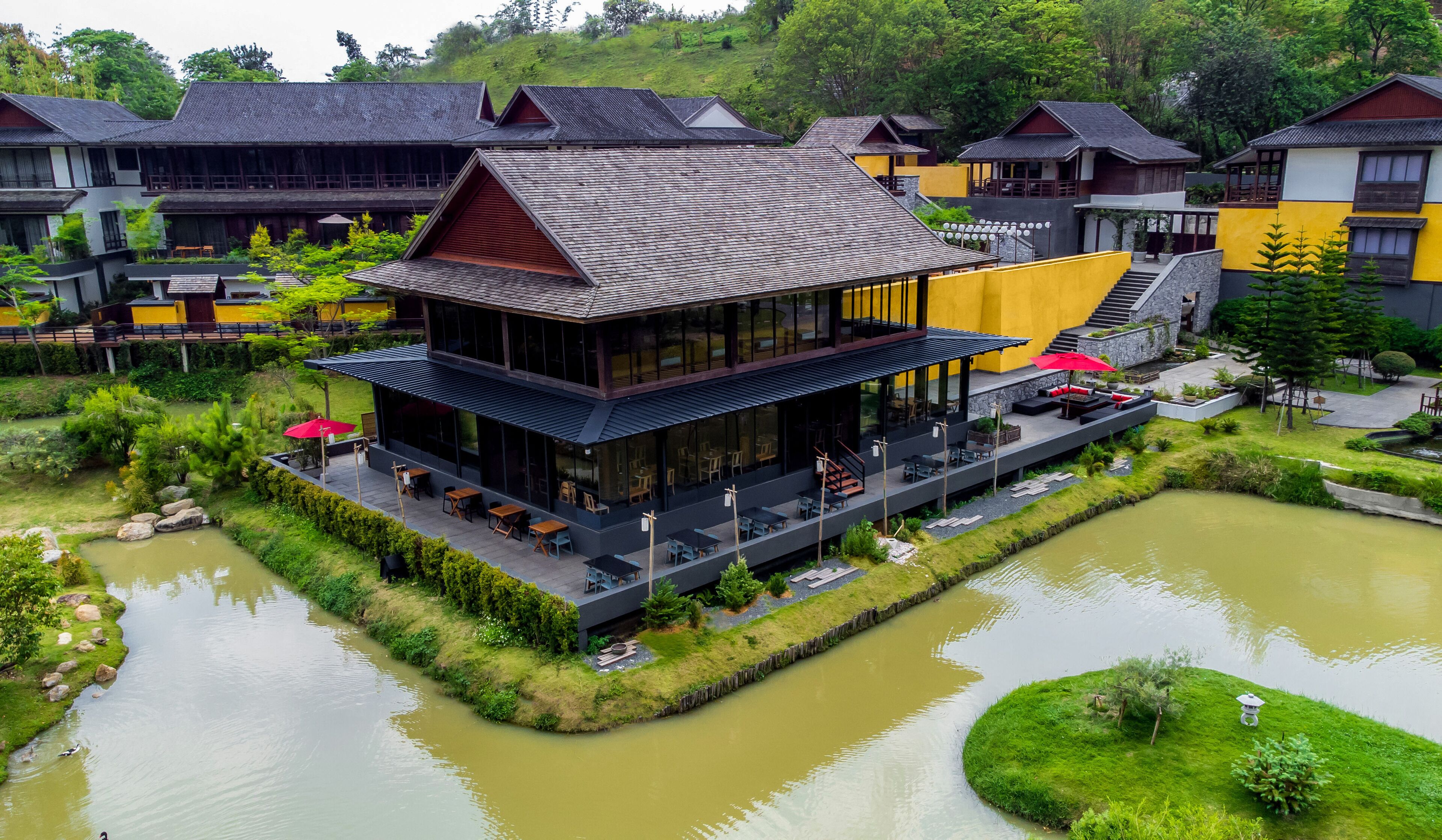 A modern building with a flat roof, large windows, and outdoor seating by a pond.